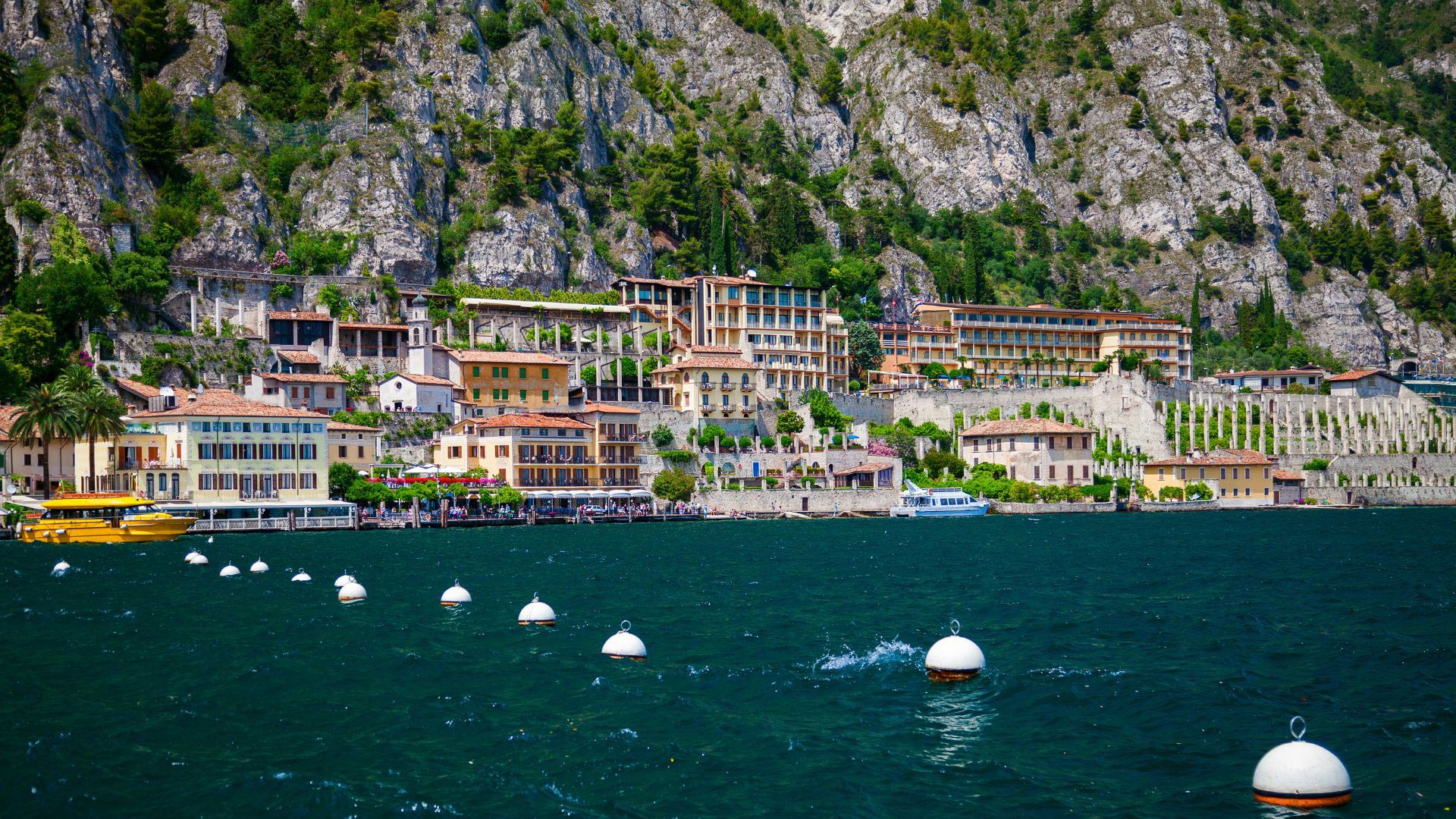 The village of Limone sul Garda seen from the lake, with pastel-colored houses along the waterfront and, on the right, the terraces with the pillars of a limonaia at the foot of the rock walls